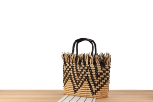Detailed macro of a woven tote bag featuring raffia fringes and geometric chevron patterns
