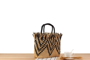 Detail of woven straw tote bag featuring bohemian tassels and a two-tone geometric pattern