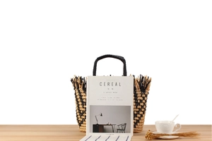 Detail of woven straw tote bag with black tassels and stripes on a rustic wooden table