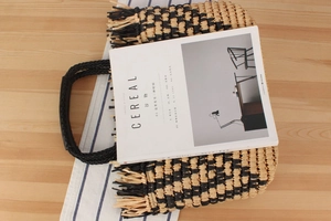 Close-up of woven straw tote bag texture with black tassels and braided handles