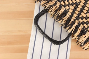Detail of woven straw tote with black leather handle grip and bohemian fringe texture