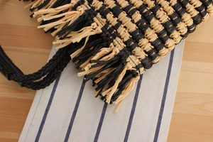 Close-up of bohemian woven bag featuring bicolor straw texture and fringe details