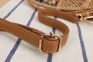 Detail of adjustable brown leather strap with gold metal buckle on woven crossbody bag