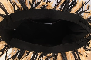 Detail view of woven straw beach bag featuring black lining, zipper and fringe trim