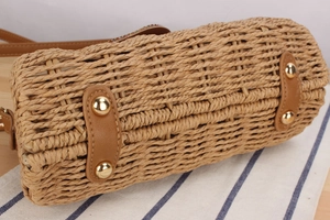 Detail of woven paper straw bag with leather accents and golden rivets on striped fabric