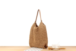 Détail du sac cabas en paille tissée avec bandoulières en cuir brun sur table en bois