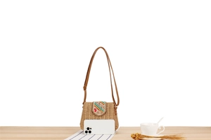 Detail of compact straw crossbody bag showing size comparison with a mobile phone