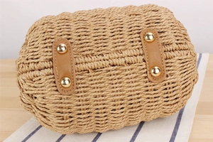 Detail of paper straw bag base featuring reinforced brown leather straps and gold rivets