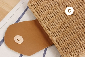 Detail of woven straw handbag featuring brown leather flap and golden magnetic clasp