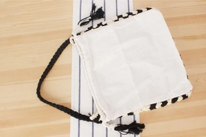Dettaglio borsa in tela bianca con bordi intrecciati bianchi e neri e coulisse con nappine