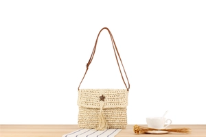 Detail of hand-woven beige straw shoulder bag with star buckle and brown fringe