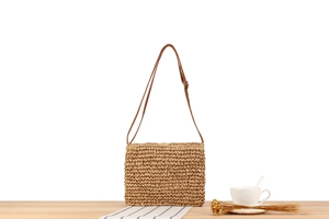 Close-up of woven straw shoulder bag featuring brown leather strap and metal buckle