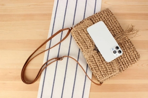 Detail of straw woven crossbody bag featuring a brown leather strap and long tassel fringe