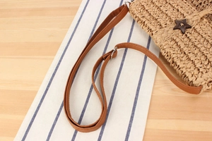 Detailed close-up of straw shoulder bag strap with brown star fastener and metal buckle