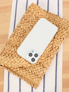 White smartphone with triple camera on straw mat, coastal vacation style flat lay