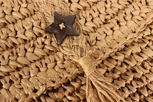 Detail of handwoven straw bag featuring a wooden star button and rustic tassel accents