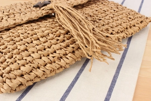 Macro shot of hand-woven straw envelope bag with decorative tassel and wooden star clasp