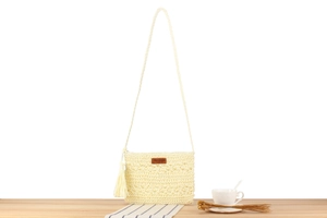 Detail einer handgefertigten Häkeltasche in Creme mit Lederlabel und Fransenquaste