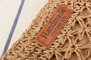 Detail eines handgefertigten Lederetiketts auf einer Strohtasche mit feiner Nahtstruktur