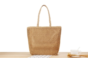 Détail d'un sac cabas en paille tissée avec doublure posé sur une table avec café
