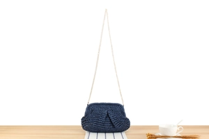 Detail of dark blue woven paper rope bag with elegant gold chain strap on wooden surface