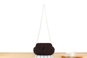 Detail of a dark brown woven clutch bag with a golden metal chain strap and retro texture