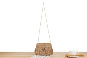 Detail of hand-woven straw crossbody bag with fine golden chain strap on wooden table