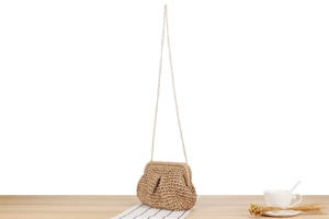 Close-up of a hand-woven straw bag with a gold chain strap on a wooden table