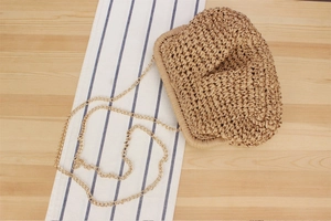 Detailed view of woven straw clutch bag with gold chain strap and textured finish