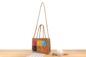 Close-up of woven straw tote bag with colorful crochet flowers on wooden surface