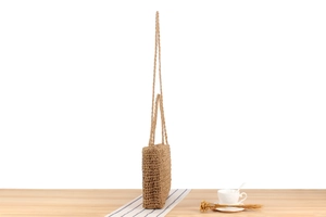Detail of hand-woven straw bag texture with long straps on a wooden table setting