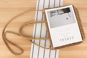 Close-up of hand-woven straw tote bag with braided handles on a wooden table