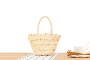 Close-up of minimalist corn husk woven handbag on a rustic wooden table for beach vacations