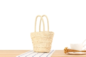 Detail of hand-woven corn husk bucket bag with dual handles on a rustic table