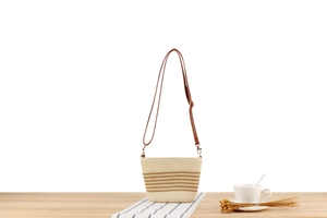 Detail of woven straw shoulder bag with brown stripes on a wooden table setup
