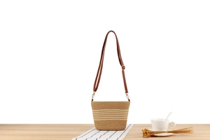 Detail of woven straw bag with horizontal stripes and brown faux leather shoulder strap