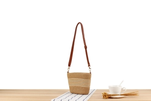 Detail of hand-woven straw bucket bag with brown leather strap on wooden surface