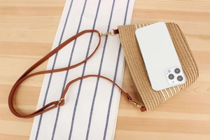 Detail of woven straw crossbody bag with leather strap next to a phone for size scale
