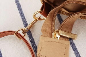Macro detail of the golden metal zipper and brown leather strap on a canvas bag