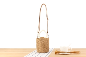 Detail of wooden bead handle and textured woven paper rope bucket bag on wooden table