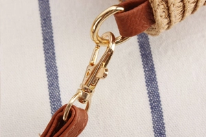 Close-up of golden metal clasp with brown leather strap and woven straw bag texture