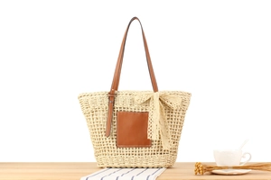 Close-up of woven straw tote bag with leather straps and beige lace bow detail