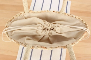 Detail view of woven straw tote bag featuring cotton linen lining and drawstring closure