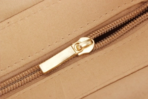Detailed close-up of a premium gold metal zipper on a khaki woven summer bag