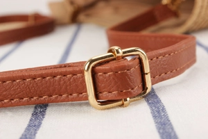Detail of brown leather strap with gold buckle and stitching on a woven straw bag