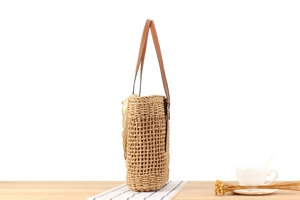 Detail of woven straw tote bag with brown leather handles on a striped tablecloth