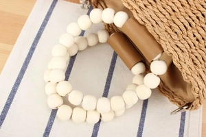 Detailed shot of woven straw handbag featuring white bead handles and leather strap accents