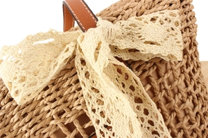 Close-up of woven straw bag detail with delicate lace bow and brown leather handle