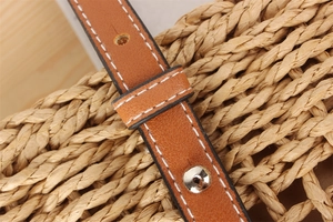 Macro detail of brown leather shoulder strap with white stitching and silver buckle on straw bag