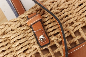 Detail of woven straw bag with brown leather strap and silver snap closure buckle